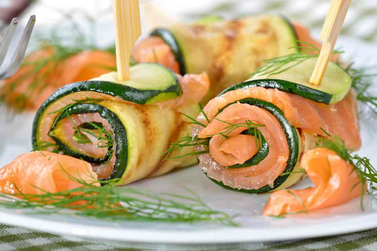 Involtini di salmone e zucchine in un piatto con foglioline di erbe aromatiche