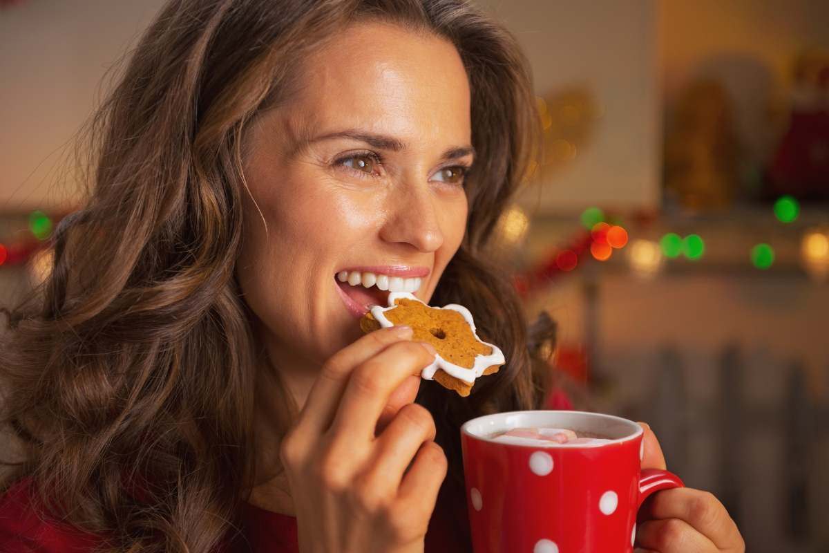 donna sorridente con una tazza in mano che mangia un biscotto