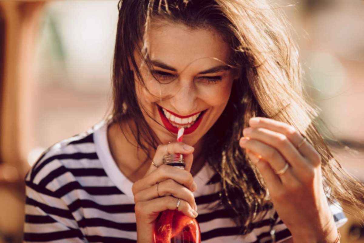donna che sorride mentre beve una bibita