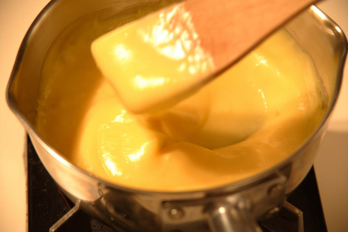 Crema pasticciera che cuoce in una pentola con mestolo di legno