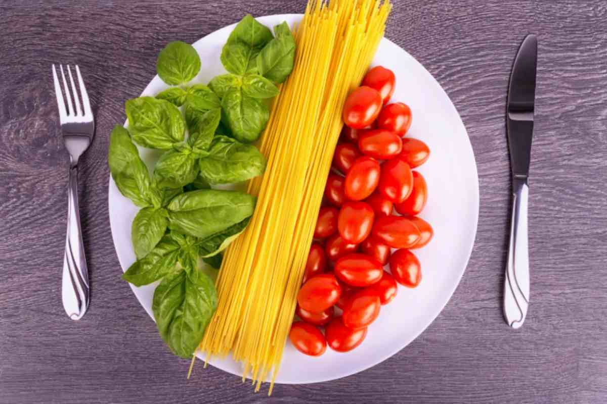 spaghetti crudi su un piatto con accanto basilico e pomodorini