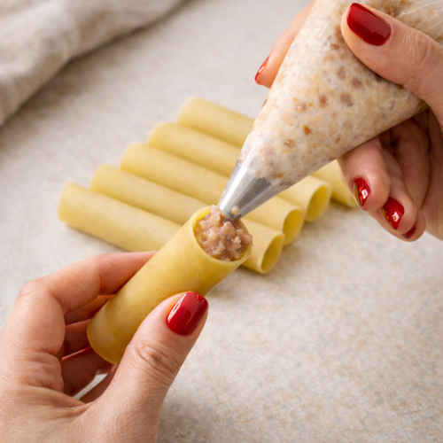 Mani di donna che farciscono dei cannelloni secchi