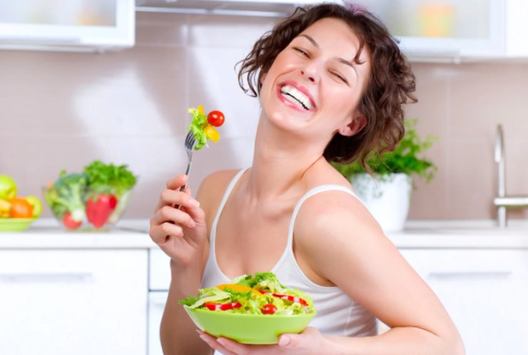 donna che sorride mentre mangia un'insalata di verdure