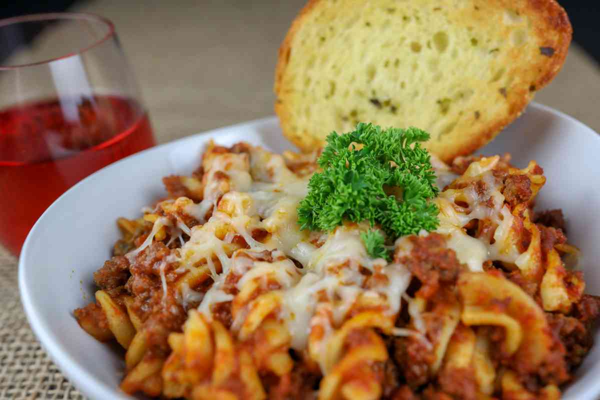 Pasta gratinata al ragù e formaggio filante in un piatto con fetta di pane