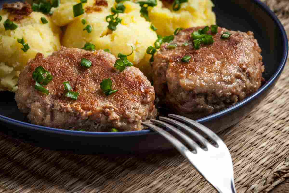 Polpette di carne schiacciate in padella con purè di patate in un piatto scuro