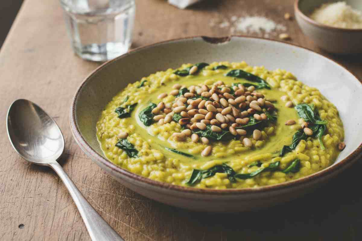 Risotto cremoso agli Spinaci, Curcuma e Pinoli tostati in un piatto su tavolo di legno