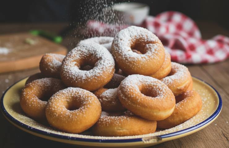Graffe fatte in casa in un piatto con zucchero a velo spolverato su