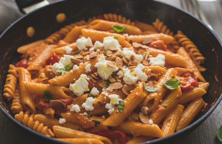 Pasta alla crema di peperoni, feta greca e mandorle tostate in una padella