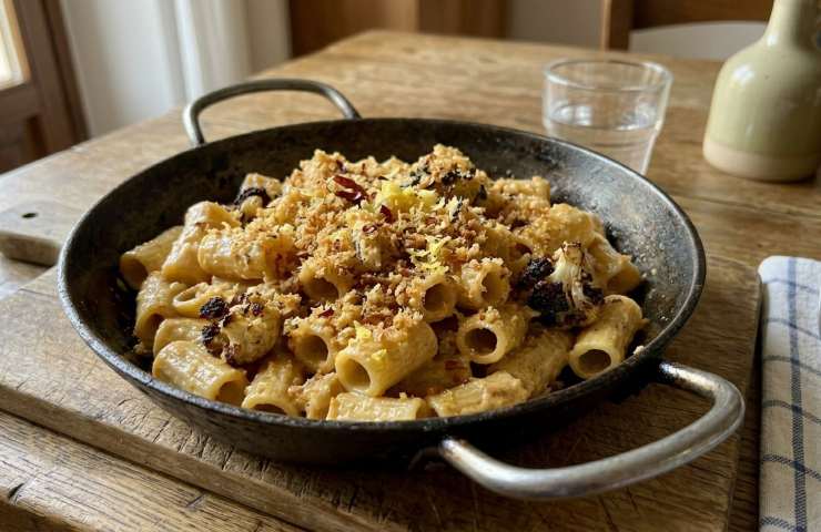 Pasta con Crema di Cavolfiore Arrostito e Briciole di Pane Aromatizzato in una padella su tagliere di legno