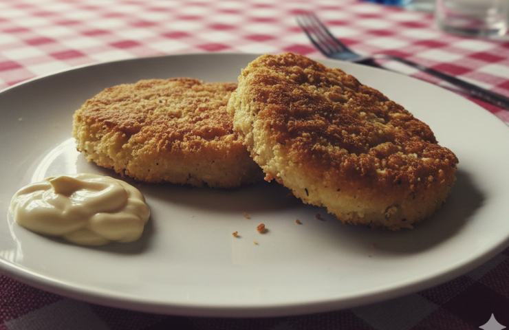 Due Cotolette di Sedano Rapa con Maionese al Lime e Pepe Rosa in un piatto su tovaglia bianca e rossa