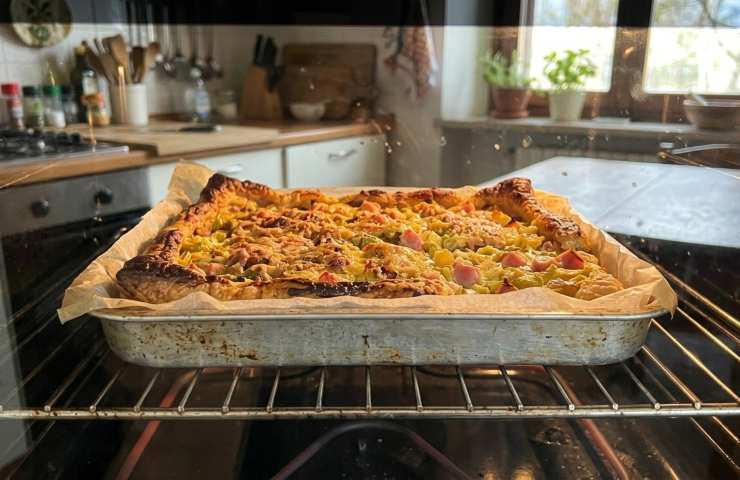 Torta salata porri e prosciutto che cuoce in forno su una griglia metallica, vista attraverso il vetro leggermente appannato.