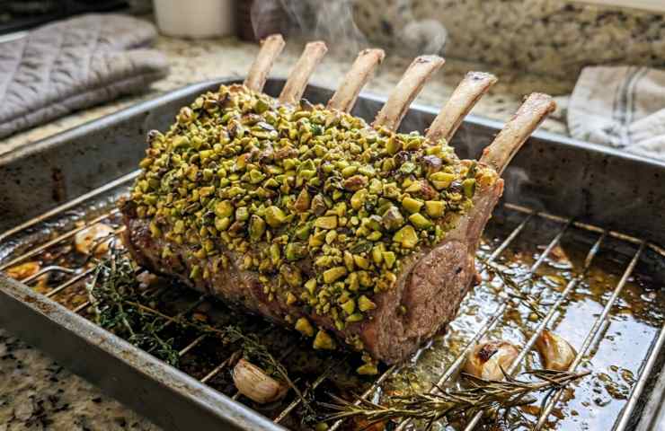 Carré di vitello in crosta di pistacchi appena sfornato, ancora caldo e fumante nella teglia da forno, pronto per il riposo prima del taglio per il pranzo pasquale.