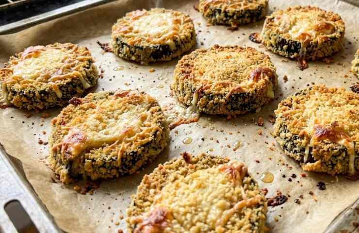 Teglia di medaglioni di melanzane al forno appena sfornati, con panatura dorata e croccante su carta forno e formaggio fuso filante.