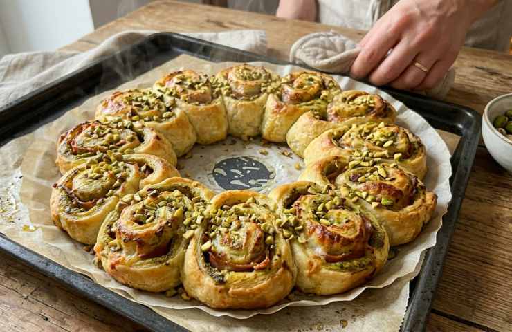 Corona di sfoglia salata appena sfornata con pistacchio e mortadella, ghirlanda rustica calda per antipasto di Pasqua.