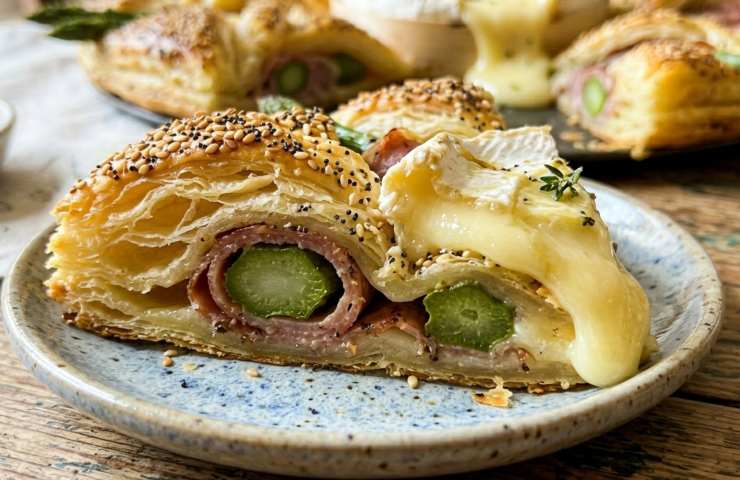 Fetta di ghirlanda di sfoglia salata con asparagi prosciutto e Camembert fuso filante e semi di sesamo ricetta antipasto Pasqua.