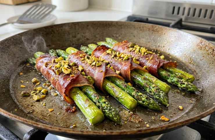 Involtini di asparagi e prosciutto crudo in padella con pistacchi dopo la cottura.