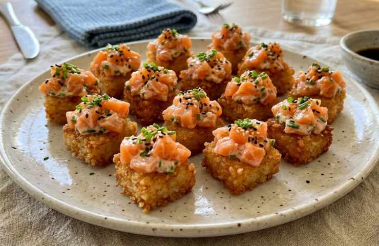 Piatto di crispy rice salmon gourmet servito su tavola apparecchiata con bacchette e salsa di soia, cubetti di riso fritto con tartare di salmone.