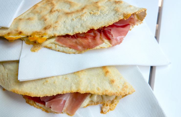 Primo piano di due piadine romagnole sovrapposte farcite con prosciutto su fazzoletti bianchi