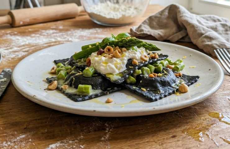Ravioli aperti neri con burrata e asparagi appena preparati in cucina.