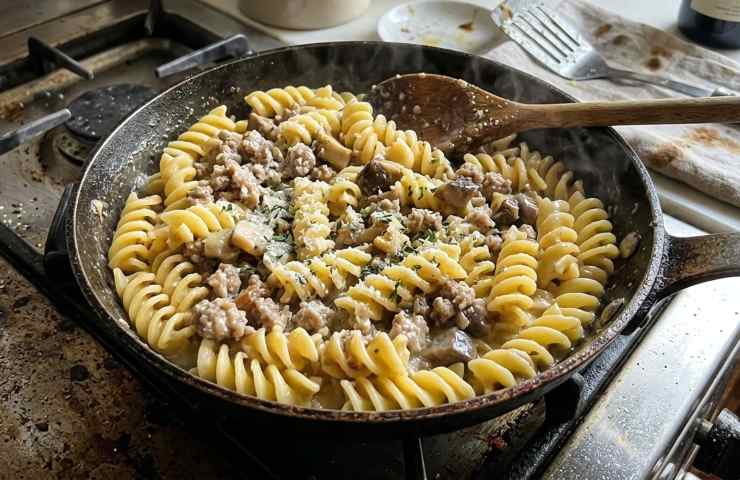 Fusilloni cremosi appena saltati in padella con ragù bianco di salsiccia e funghi porcini fumanti, pronti per essere serviti durante un pranzo casalingo.