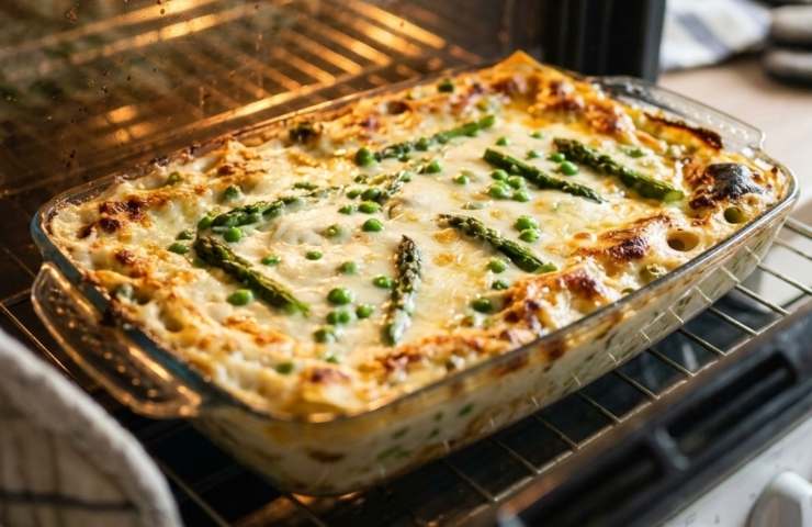 Lasagna asparagi e piselli cotta in una teglia in forno con luce accesa