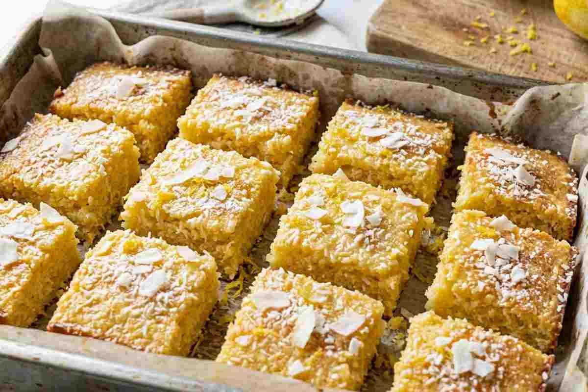 Quadrotti soffici al limone e cocco appena sfornati in teglia, spolverati con cocco rapé e scorza di limone fresca.