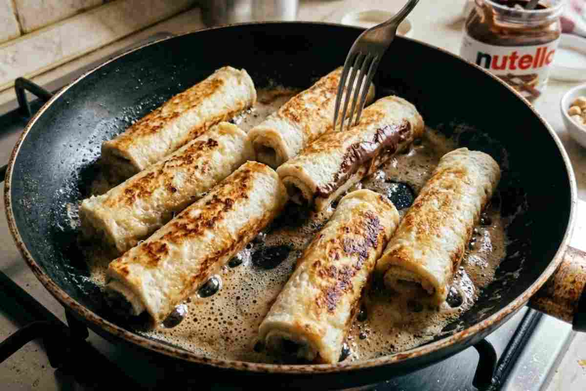 Rotolini di pancarré alla Nutella mentre dorano in padella con burro sfrigolante, scatto ravvicinato in cucina.