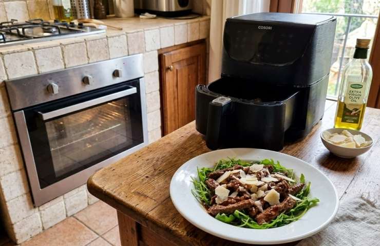Filetti di salmone in crosta di pistacchi pronti sul tavolo della cucina, con friggitrice ad aria accesa e forno a microonde visibili sullo sfondo.