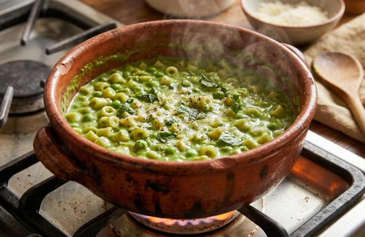 Pasta e piselli cremosa fumante in pentola di coccio rustica sul fuoco.