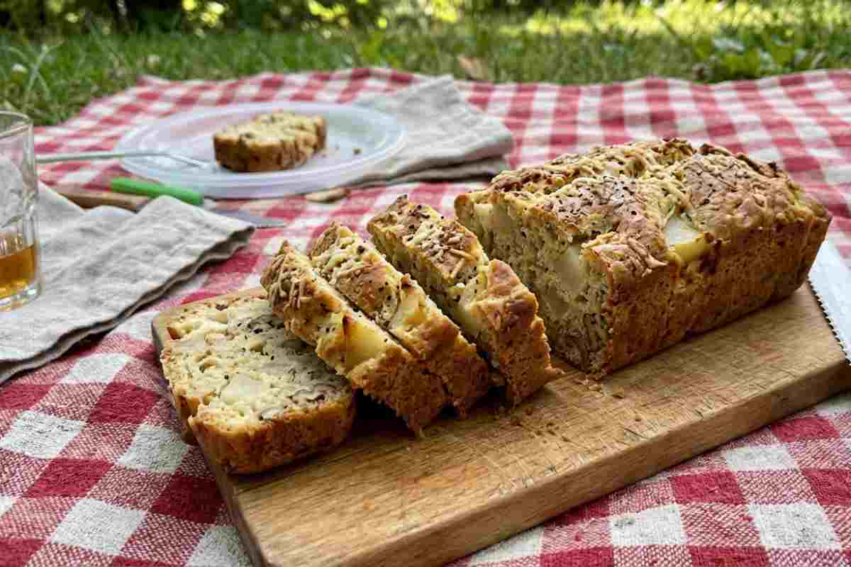 Plumcake salato cacio, pepe e pere a fette su tagliere durante un picnic di Pasquetta.