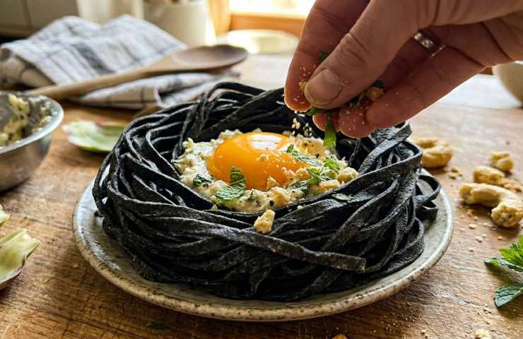 Preparazione del nido di Pasqua con crespelle nere, ricotta e aggiunta del tuorlo d'uovo fresco.