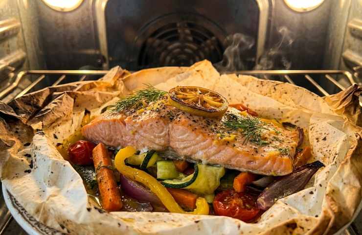 Salmone al cartoccio in cottura nel forno ventilato con verdure e carta forno dorata.