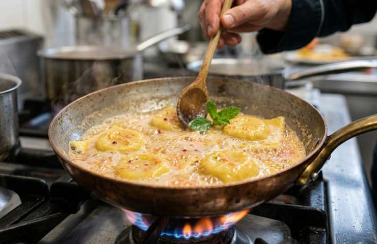 Ravioli fatti in casa che saltano in padella con una riduzione di pompelmo rosa e burro chiarificato, durante la mantecatura finale con pepe rosa.