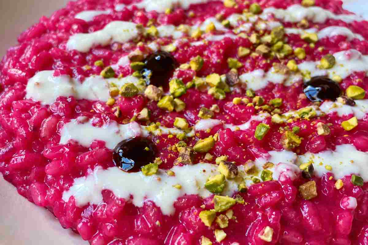 Risotto alla barbabietola cremoso con crema di caprino e pistacchi, piatto fucsia impiattato all'onda visto dall'alto.