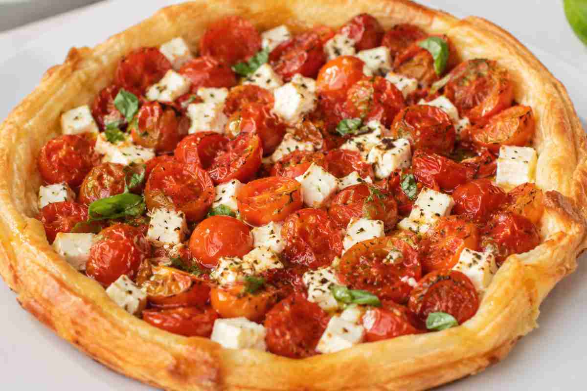 Tarte Tatin salata con pasta sfoglia croccante, pomodorini arrostiti, feta e basilico fresco su piatto bianco, primo piano luminoso e realistico.