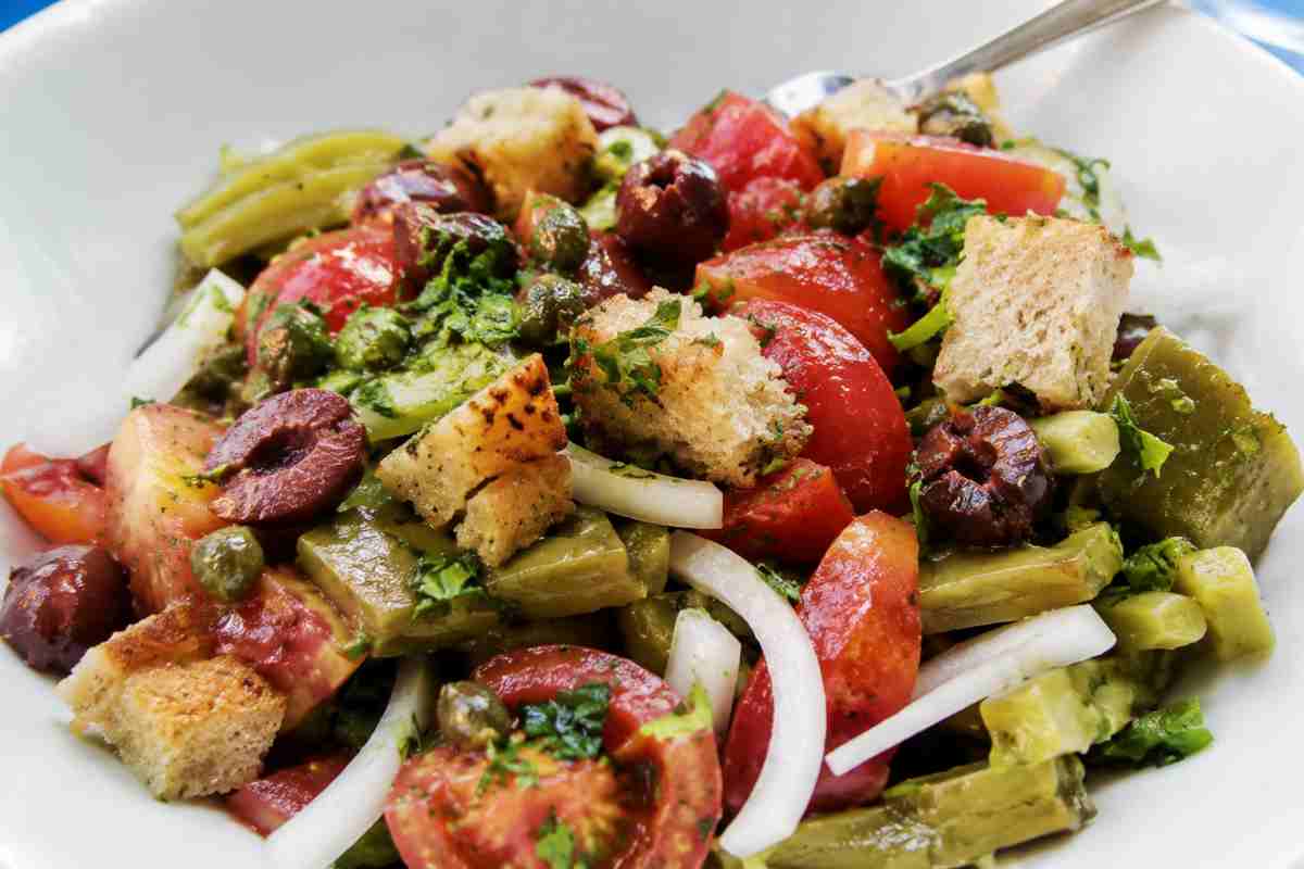 Insalata alla Pantesca tradizionale con pomodori freschi, patate, capperi di Pantelleria, olive nere e cipolla rossa in una luminosa fotografia mediterranea ravvicinata.